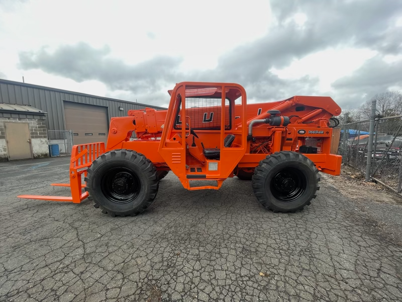 An orange forklift is parked in a parking lot in front of a building.