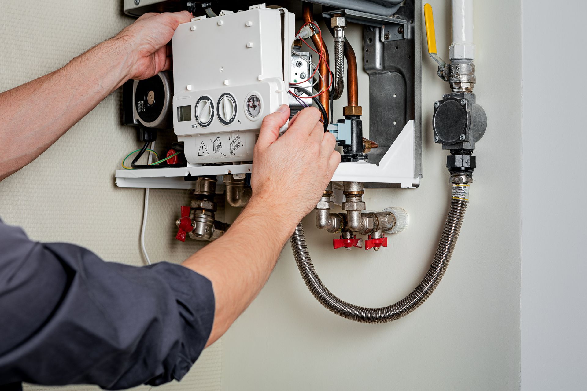 Technician repairing an open wall-mounted boiler with exposed pipes and controls