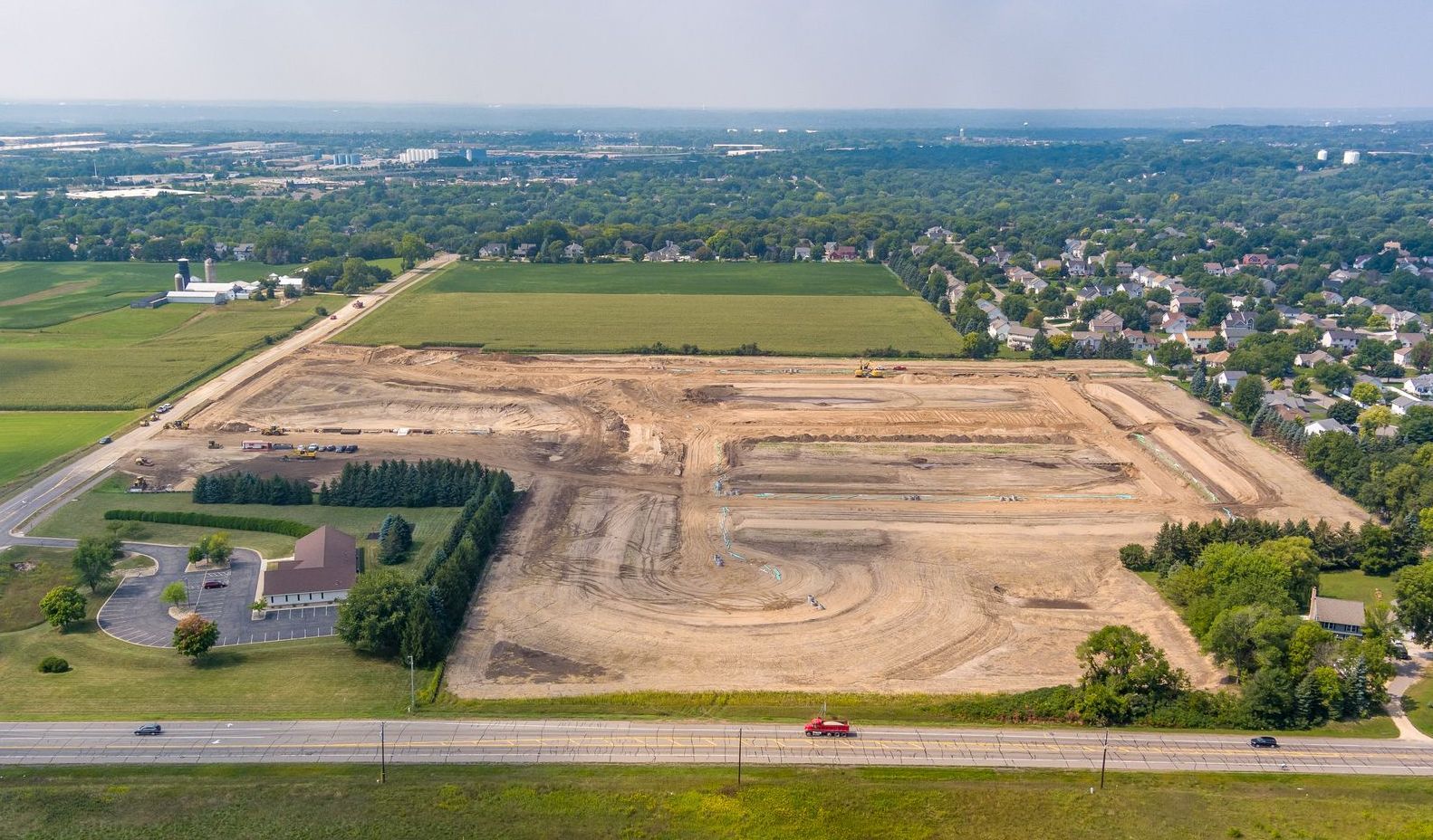 Aerial view of a large construction site with excavated earth, bordered by roads and green fields.