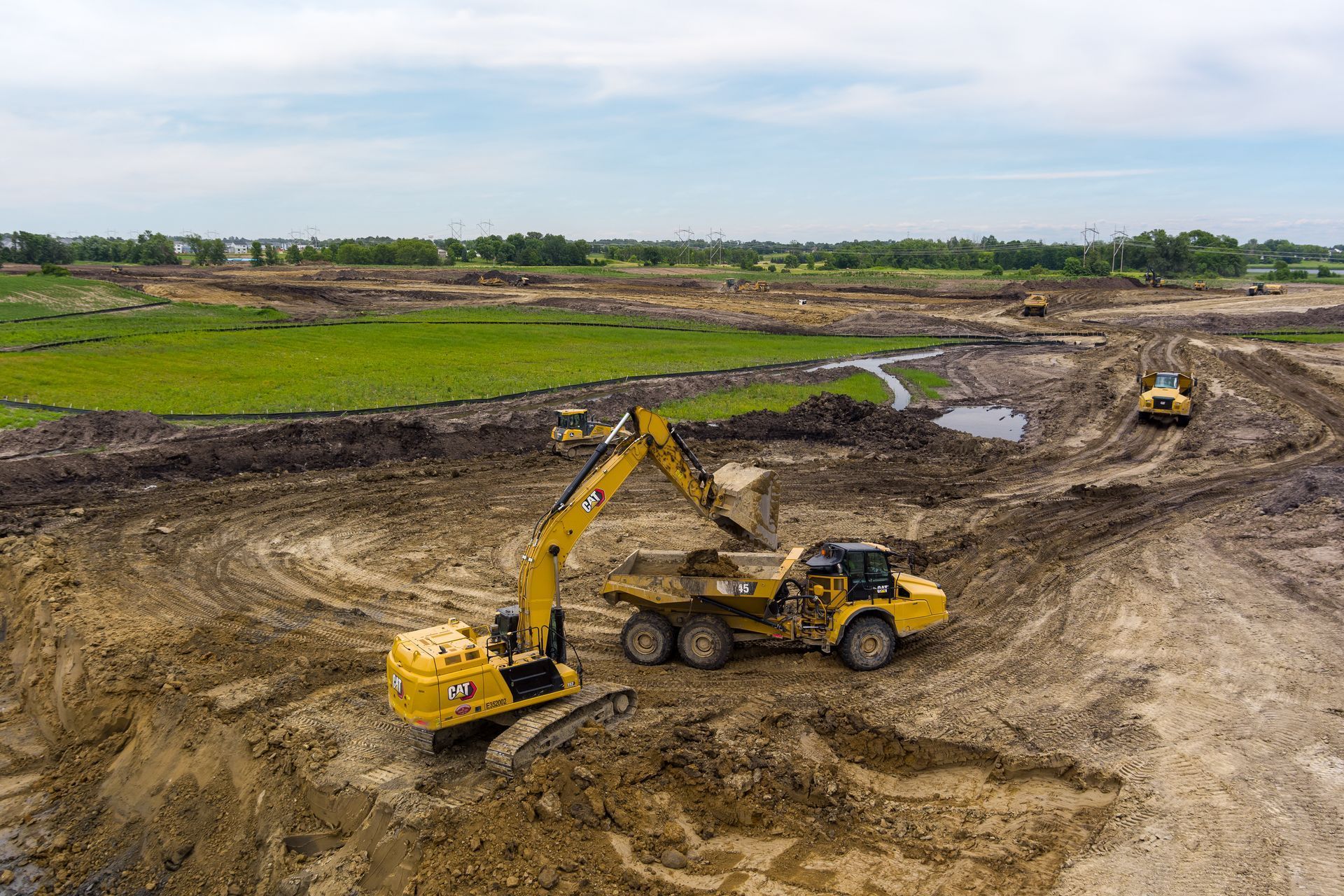 Yellow excavator loading a dump truck at a construction site. Dirt and heavy equipment on a cloudy day.