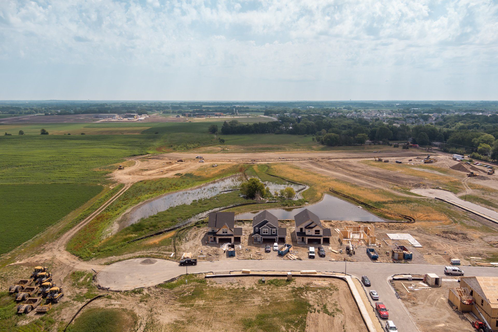 Construction site with houses under construction, ponds, and fields.