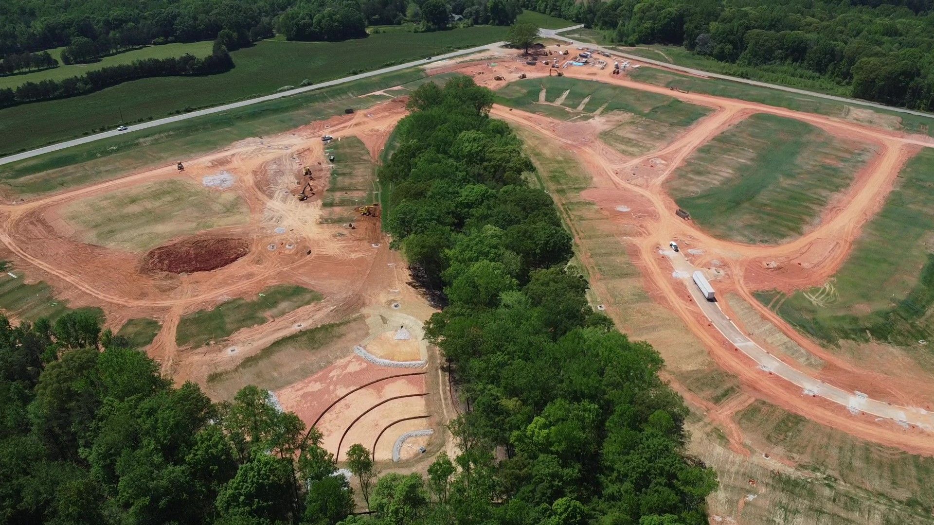 Aerial view of a construction site with cleared land, terraced areas, and an amphitheater.