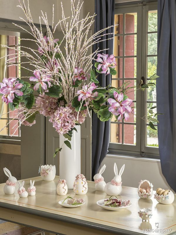 Un vaso pieno di fiori rosa si trova su un tavolo vicino a una finestra.