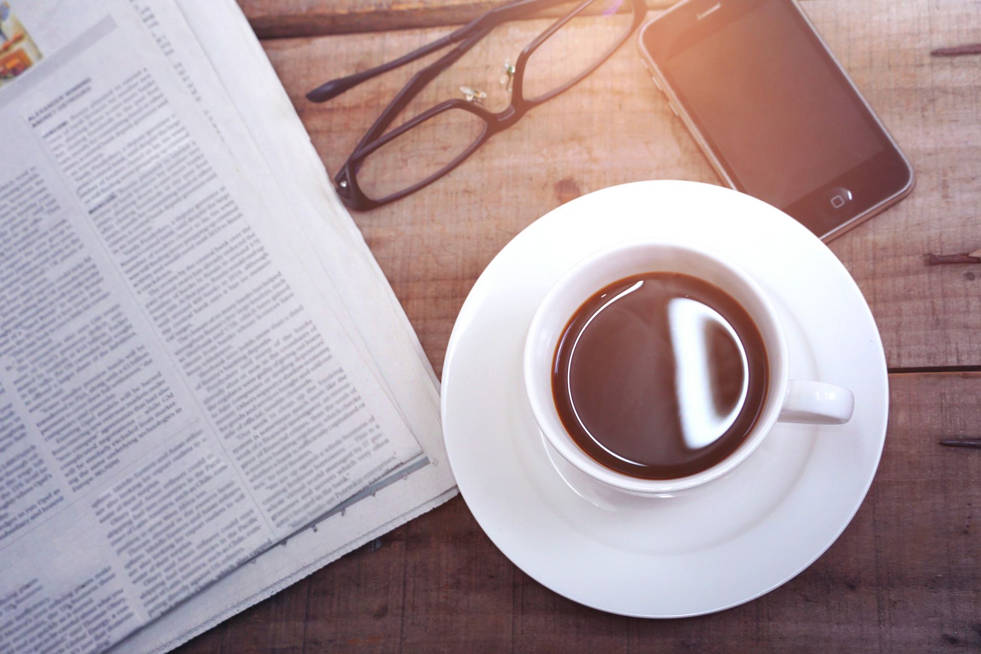 Open book, eyeglasses, tablet, and a cup of coffee on a wooden desk