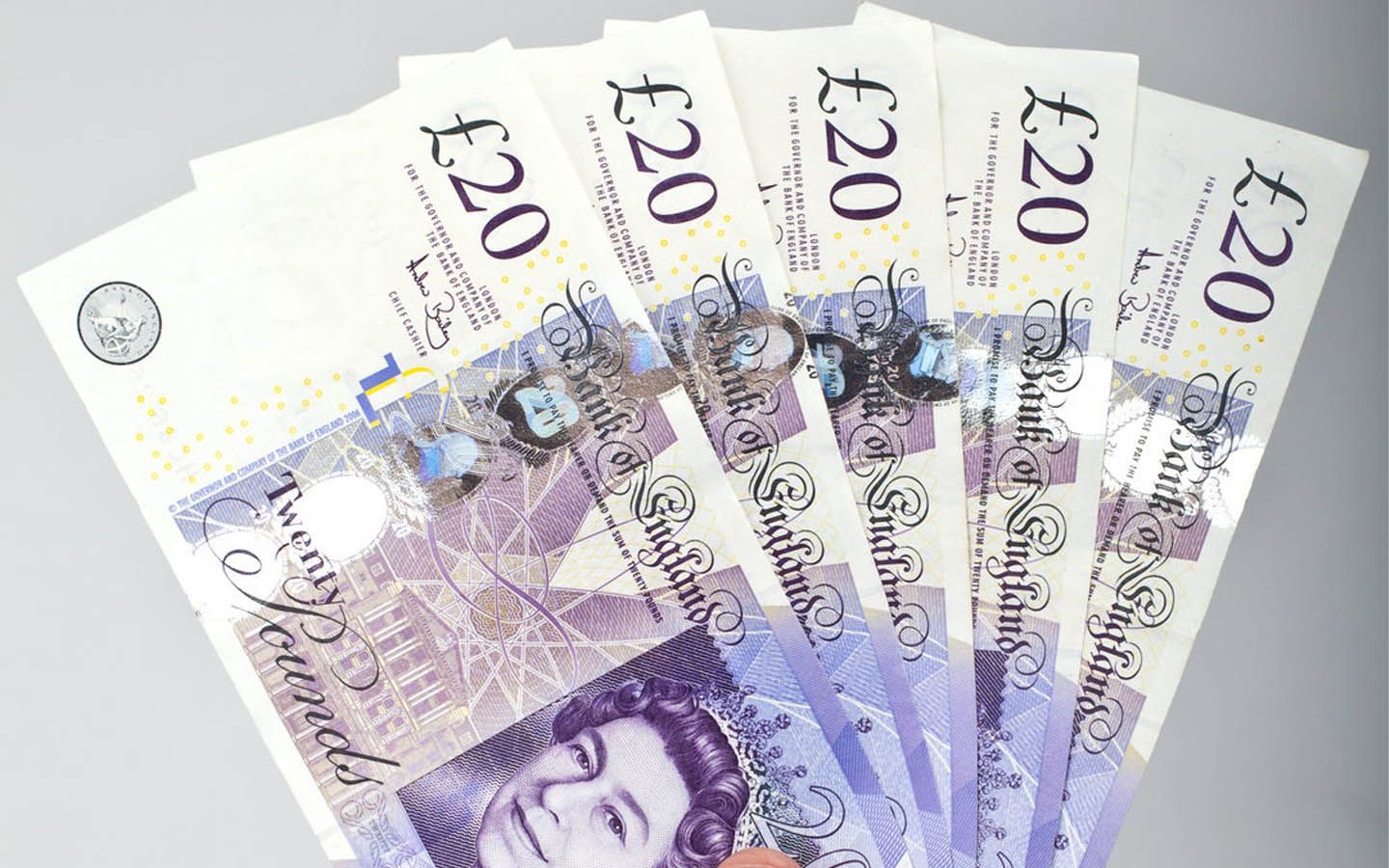A fan of 20 pound notes on a gray surface.