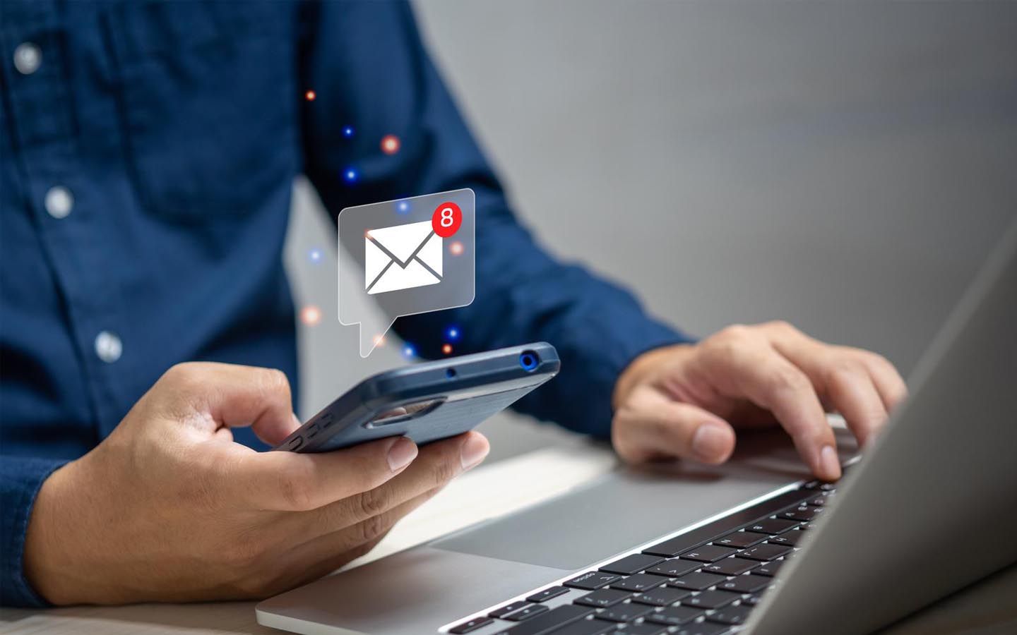 A man is using a laptop computer while holding a mobile phone.