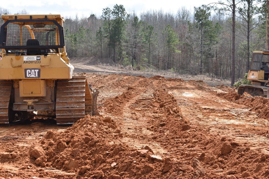 A bulldozer is driving down a dirt road next to a tractor.