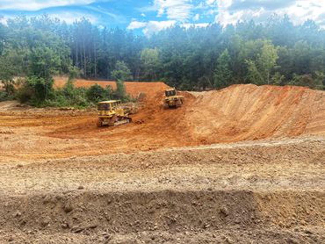 Two bulldozers are working in a dirt field.