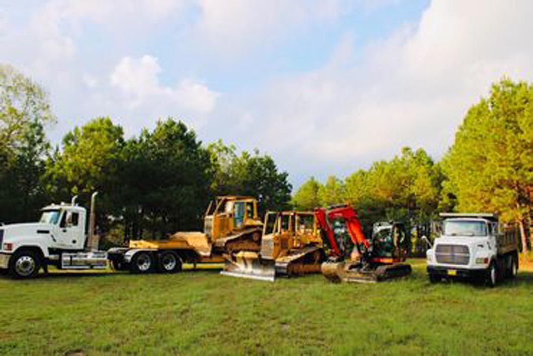 A group of construction trucks are parked in a grassy field.