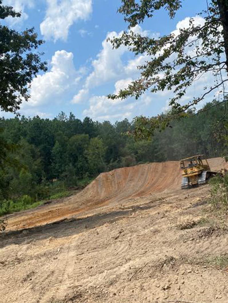 A bulldozer is driving down a dirt road in the middle of a forest.