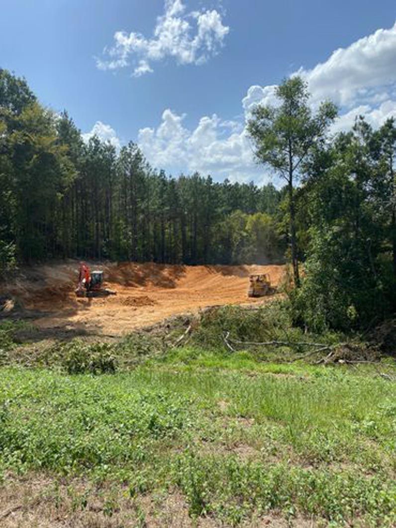A large dirt field with trees in the background and a bulldozer in the foreground.
