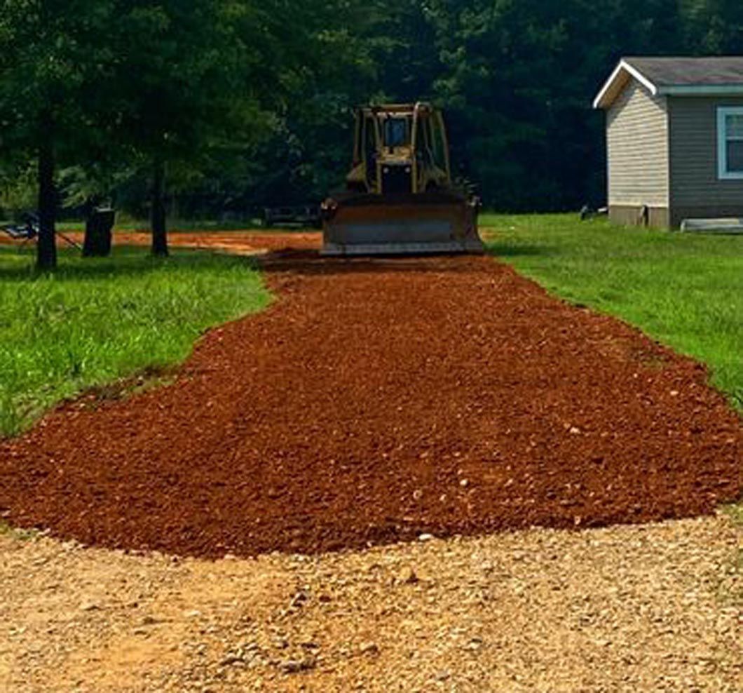 A bulldozer is driving down a dirt road next to a house.