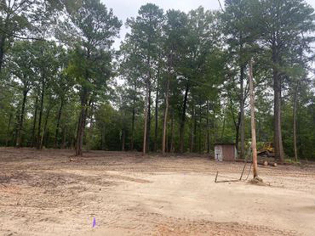 A dirt field in the middle of a forest with trees in the background.