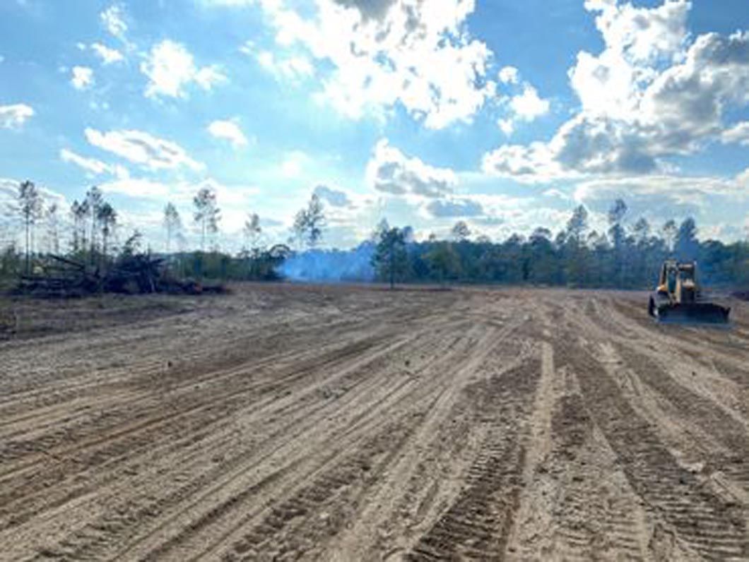A bulldozer is driving down a dirt road next to a forest.