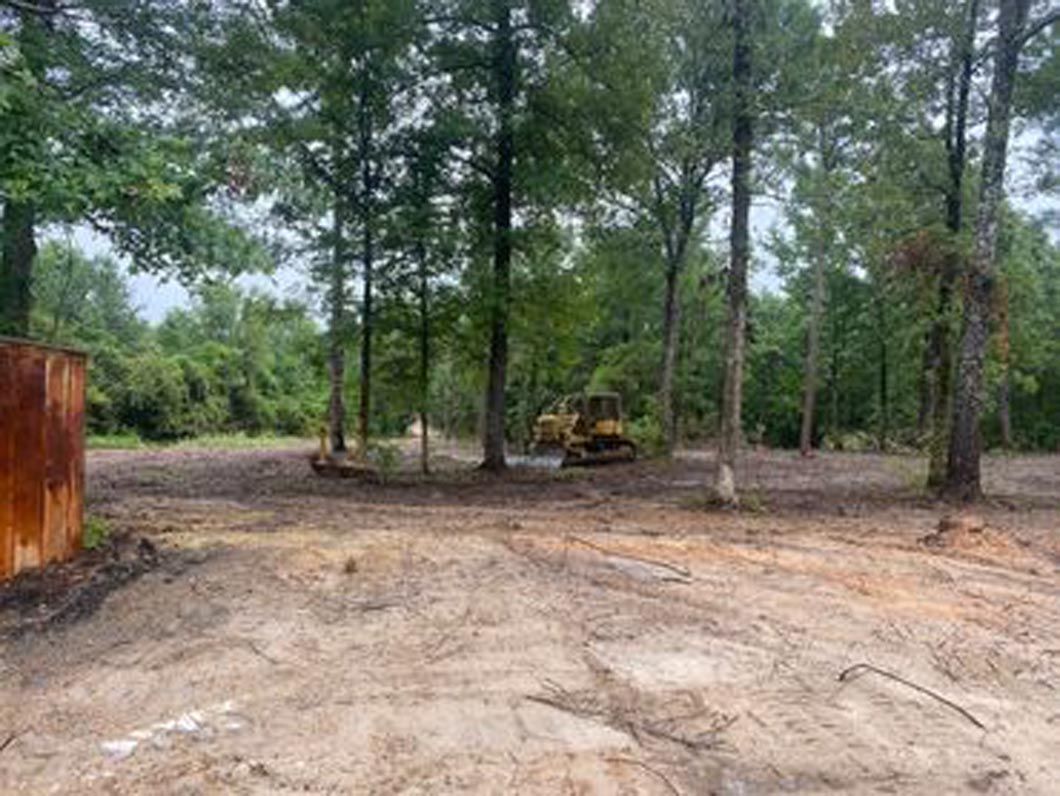 A bulldozer is driving through a dirt field surrounded by trees.