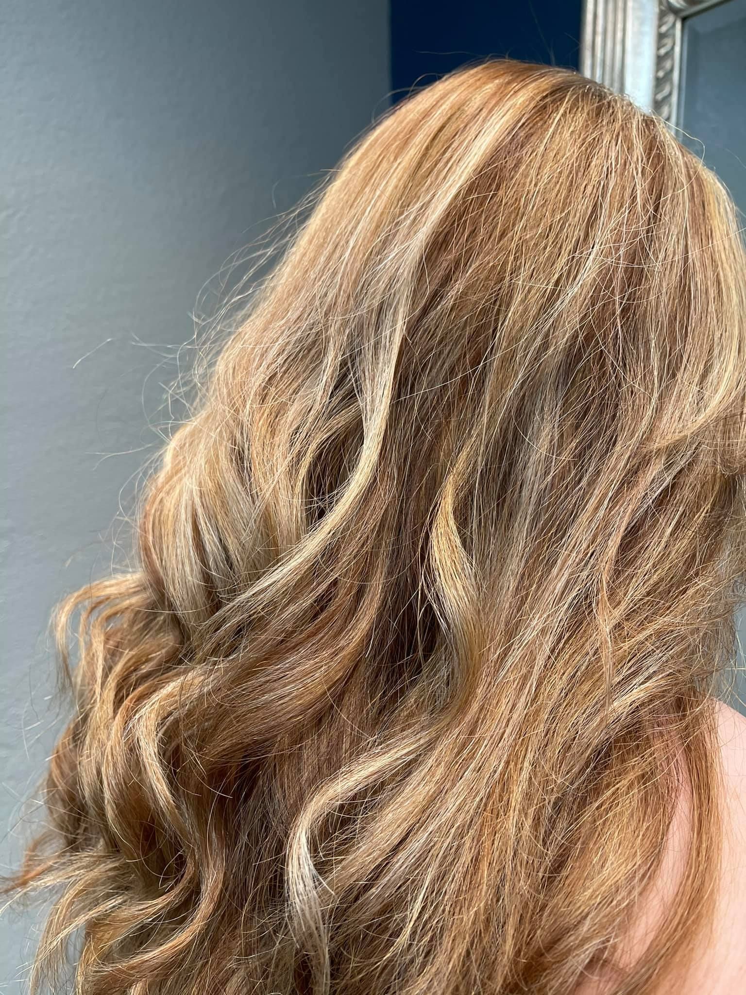 Wavy, highlighted blonde hair cascading down, next to a silver framed mirror.