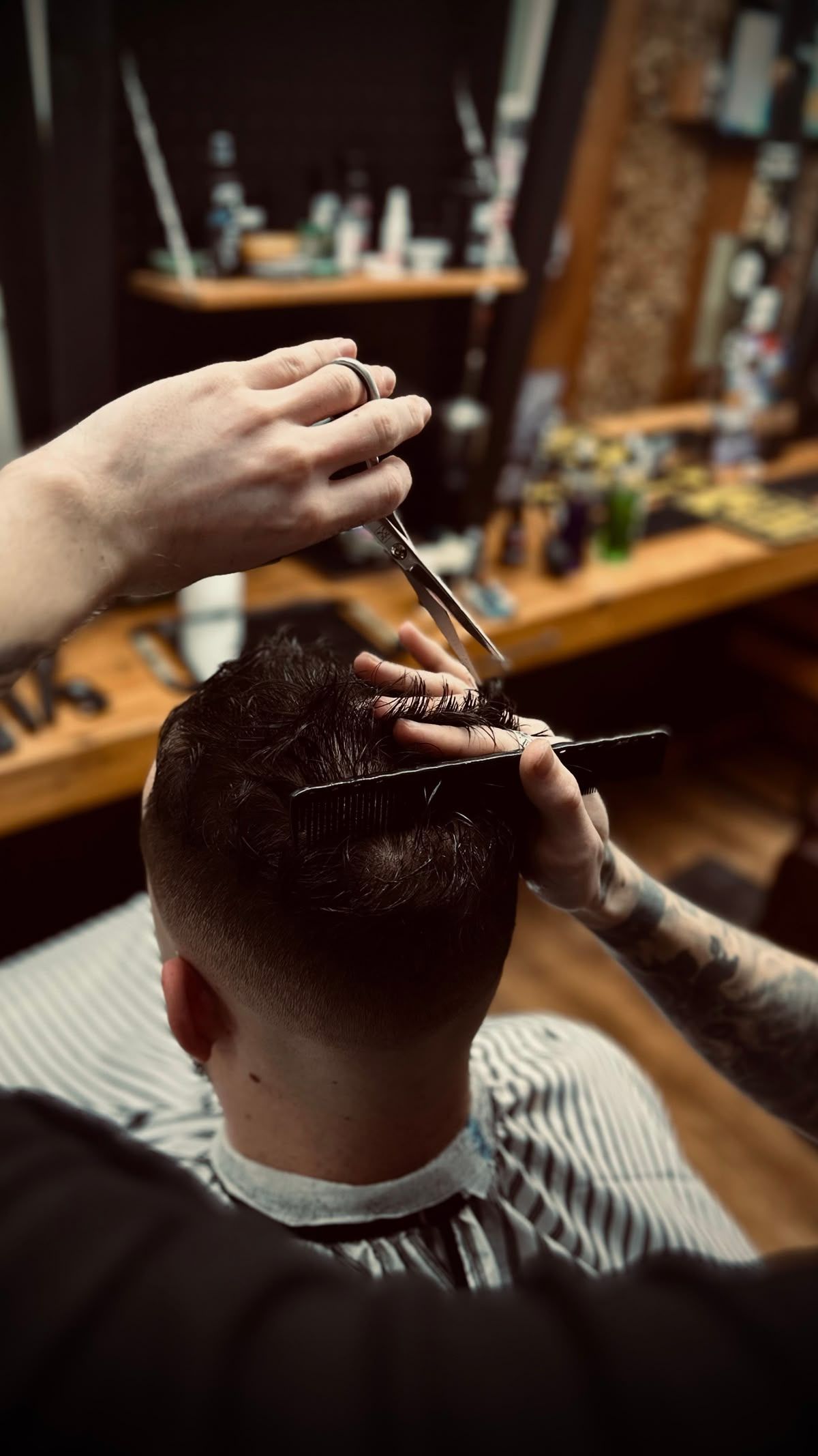 A barber giving a haircut. Hands hold scissors and comb, trimming dark hair in a barber shop.