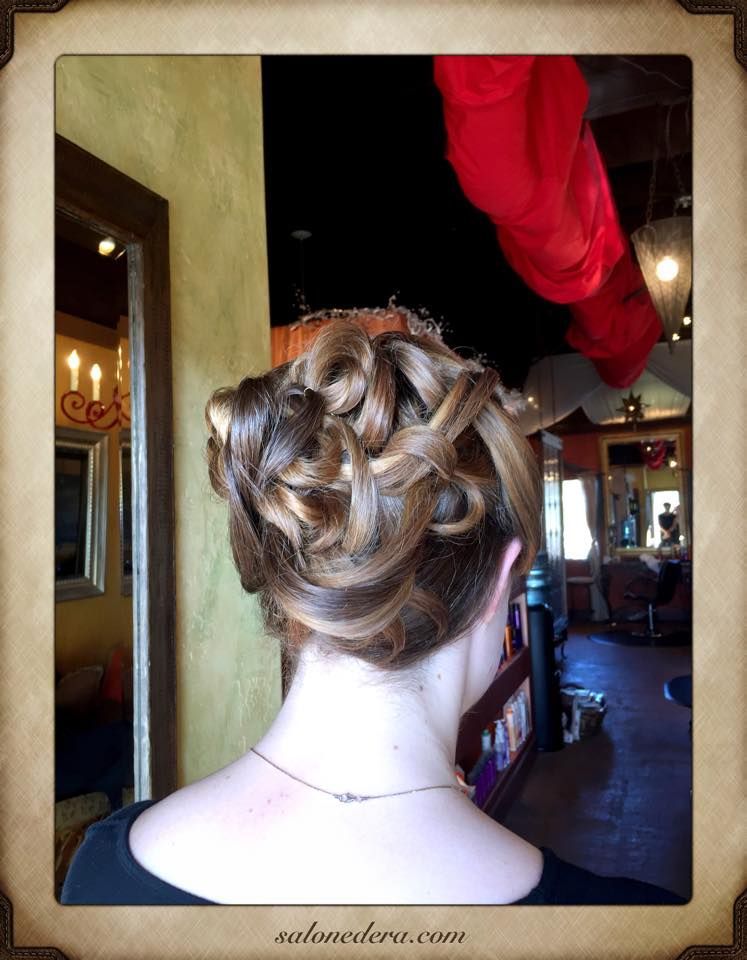 Woman with brown hair in an updo, back view. Hair is styled with curls and twists. Setting appears to be a salon.