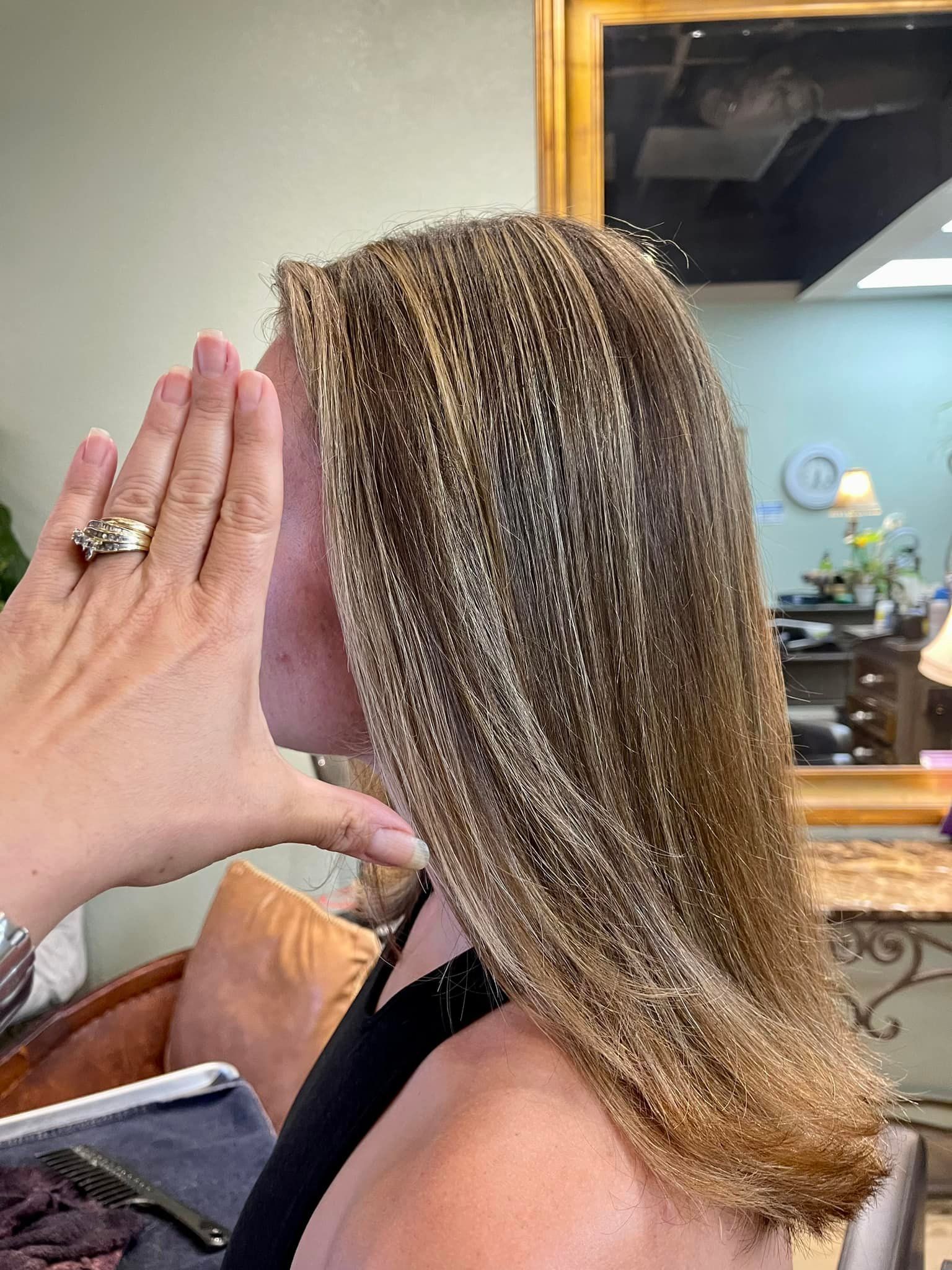 Woman with highlighted hair at a salon, hand is near her face; in the background, a mirror and salon decor.