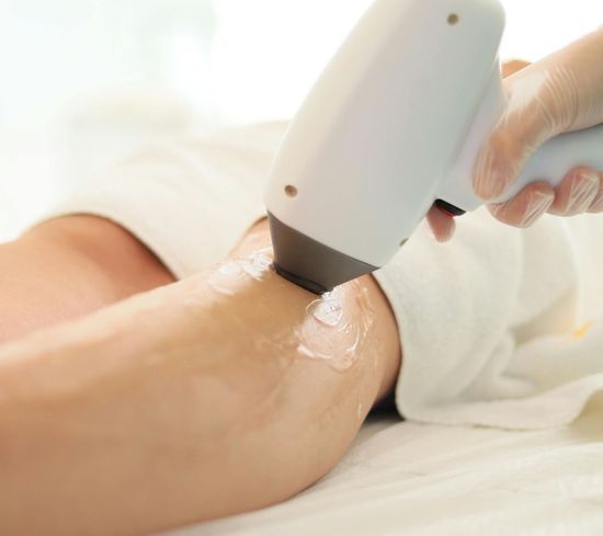 A person receiving laser hair removal on their leg. A technician holds a device over the treated area.
