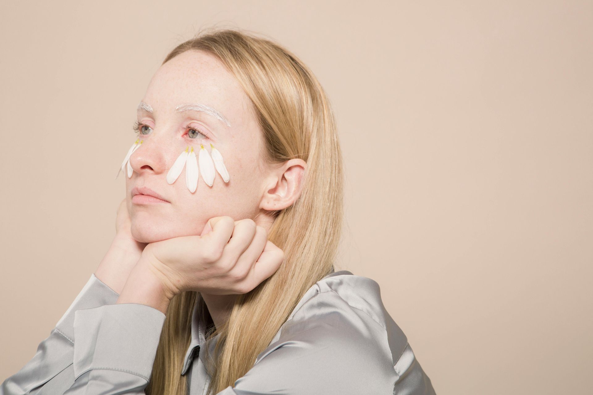 Blonde woman with daisies around her eyes and a cream-colored face mask.