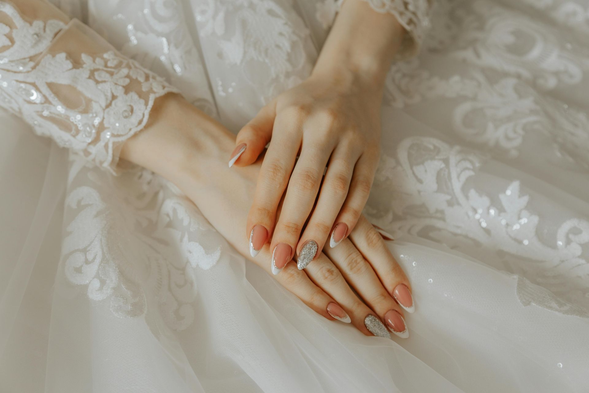 Woman's hands with French tip nails resting on a white lace wedding dress.