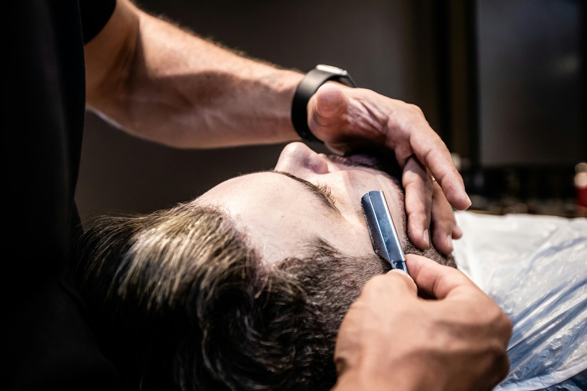 Barber shaving a client's face with a straight razor; close-up view in a barbershop.