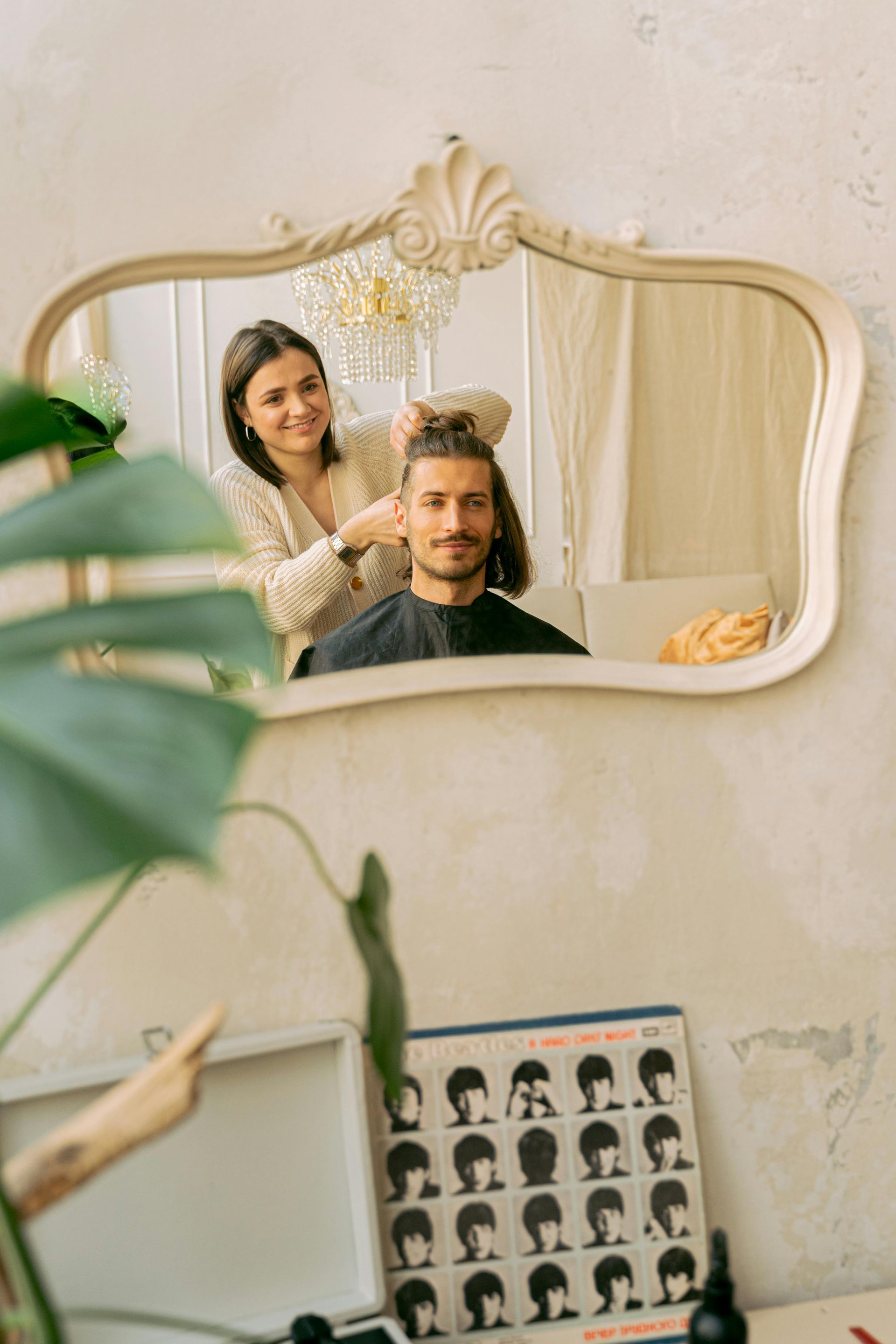A person getting a haircut in a salon. A stylist with a smile cuts a man's hair in front of a mirror.