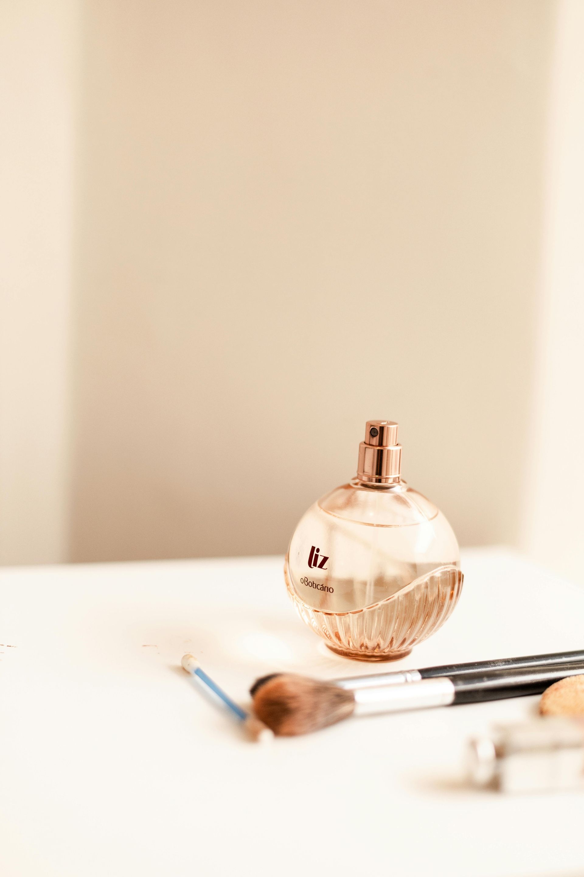 A perfume bottle and makeup brushes on a white surface, against a neutral background.