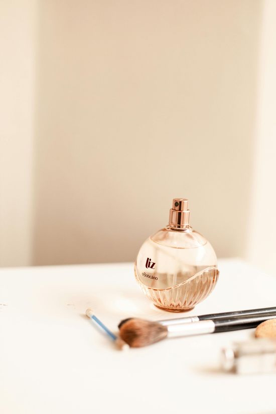 A perfume bottle and makeup brushes on a white surface, against a neutral background.