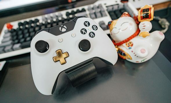 A white xbox controller is sitting on a table next to a lucky cat figurine.