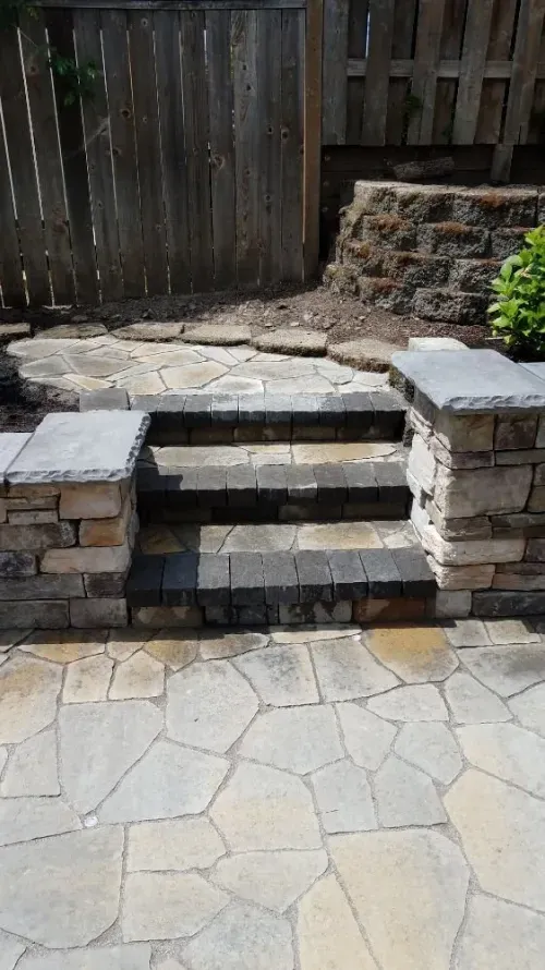 A stone patio with stairs and a wooden fence in the background.