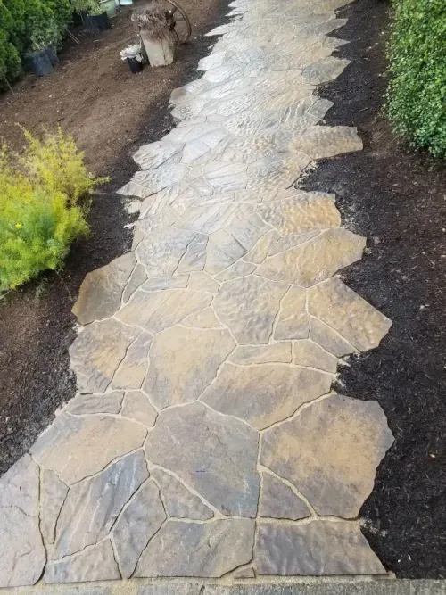 A stone walkway in a garden with a bench in the background.