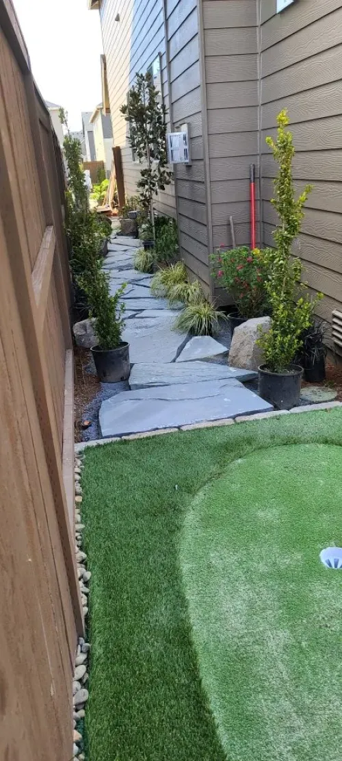 A stone walkway leading to a backyard with a fence and grass.