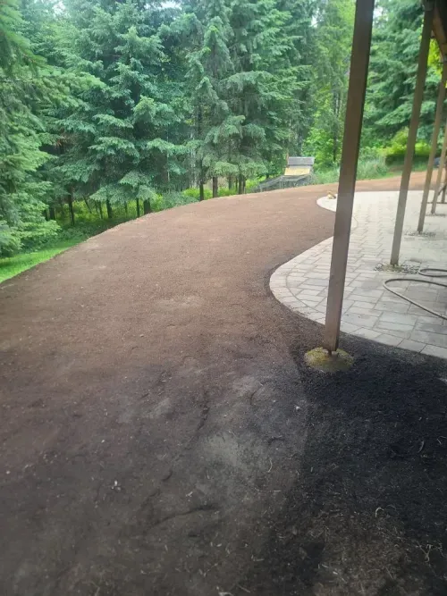 A dirt road leading to a patio with trees in the background.