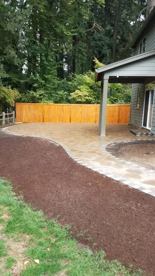 A house with a wooden fence and a patio in front of it.