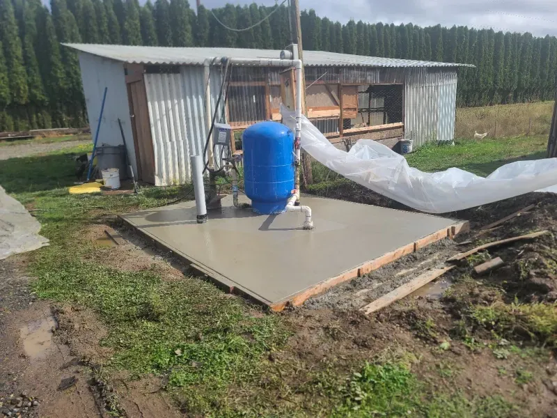 A blue tank is sitting on top of a concrete platform in front of a shed.