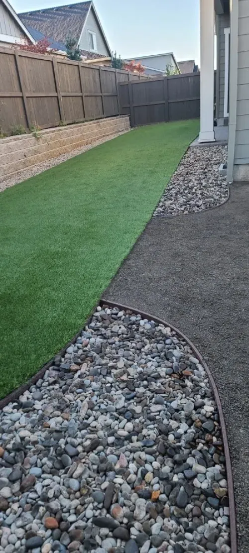 A lawn with a fence and a walkway surrounded by rocks and grass.