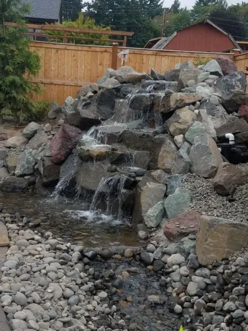 A waterfall is surrounded by rocks and a wooden fence.