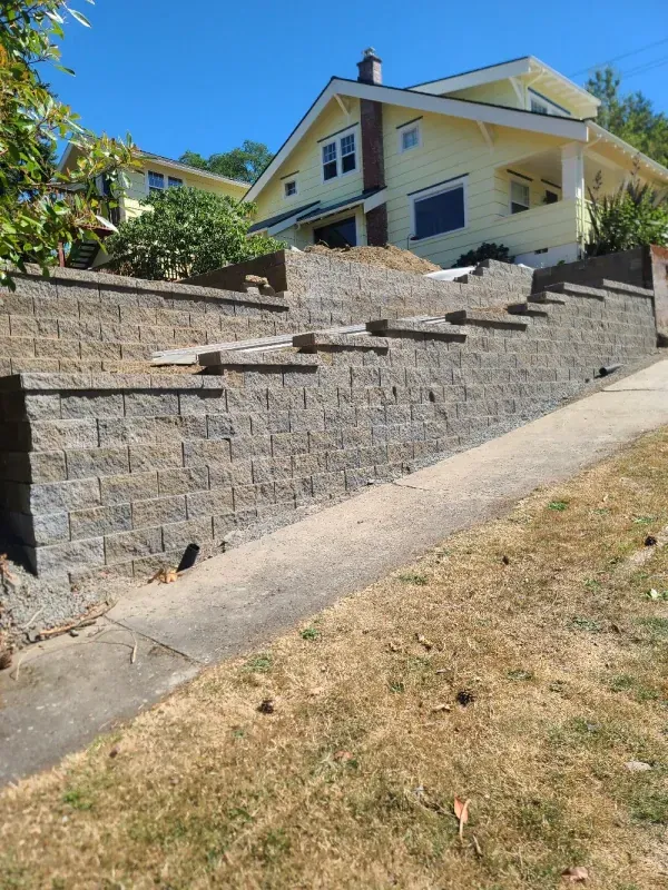 A large house is sitting on top of a hill next to a brick wall.