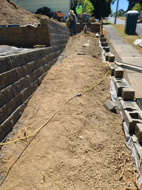 A man is working on a retaining wall next to a sidewalk.