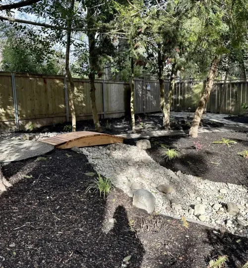 A wooden fence is surrounded by trees and rocks in a garden.