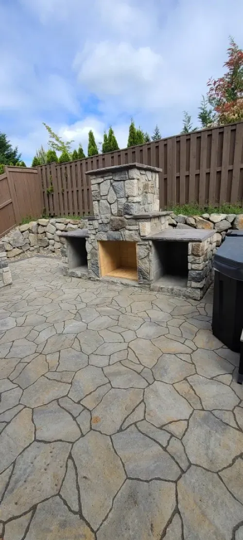 A stone fireplace is sitting on a patio next to a wooden fence.