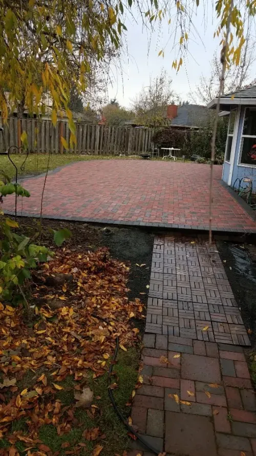 A brick driveway leading to a house with leaves on the ground.