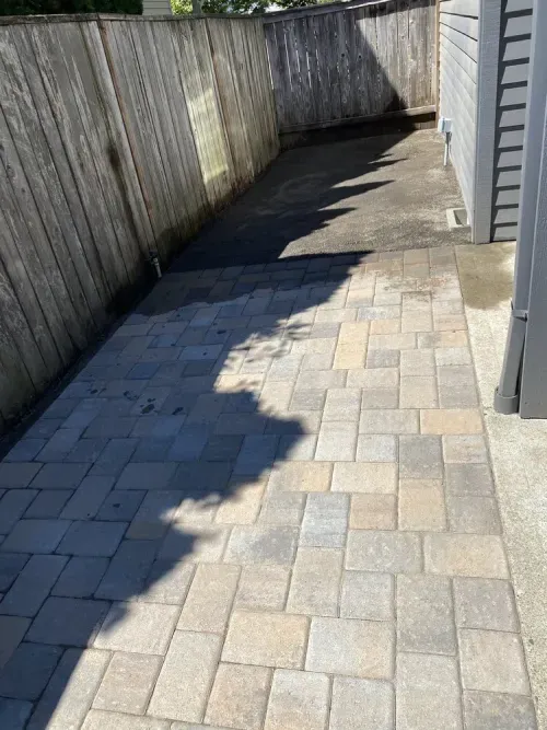A brick walkway leading to a house with a wooden fence.