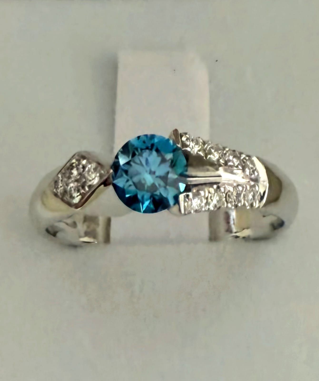 Anello con pietra preziosa blu e dettagli in diamante su sfondo bianco.