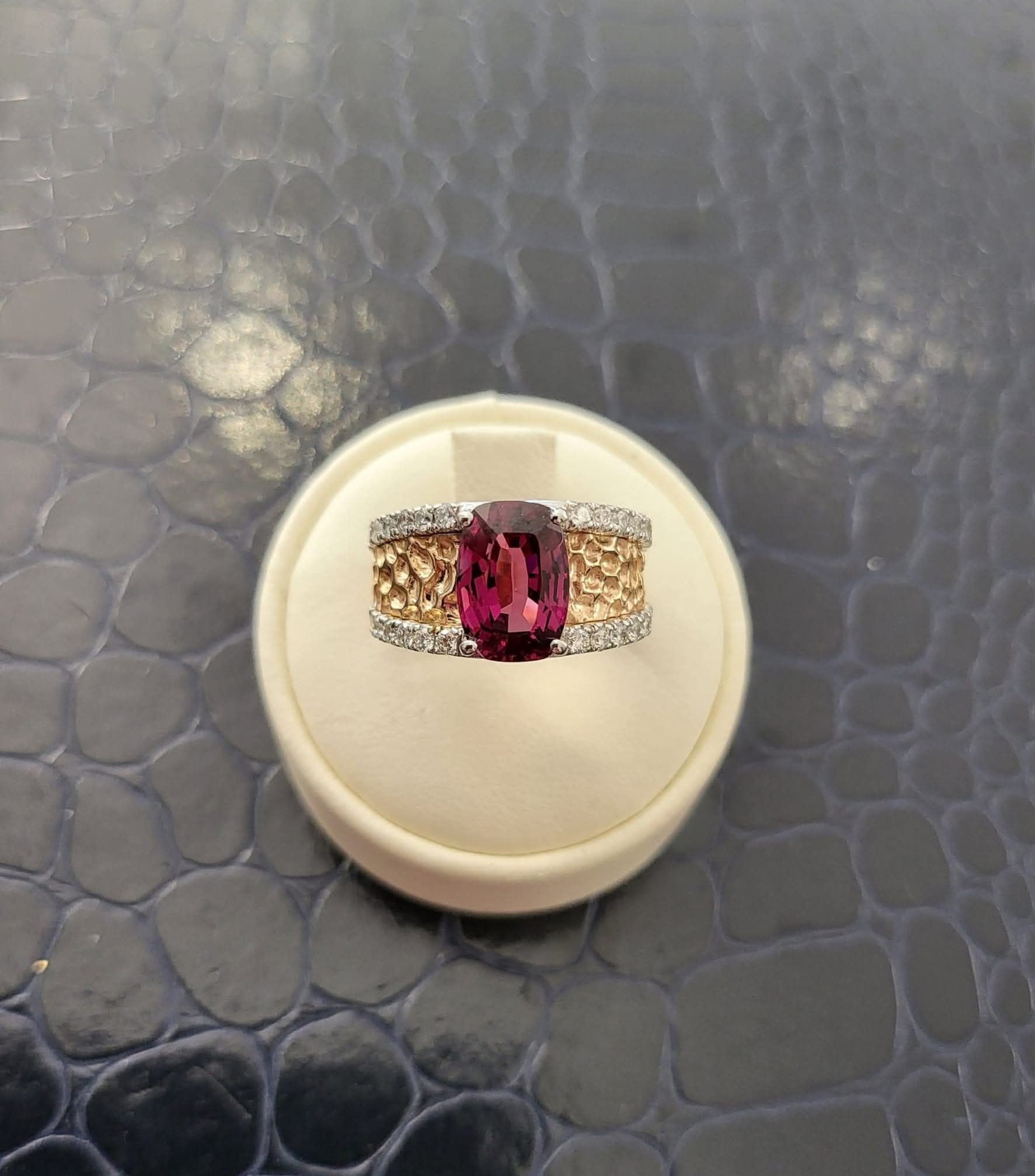 Anello con grande pietra preziosa rosa rettangolare, dettagli in oro e diamanti, su supporto bianco.
