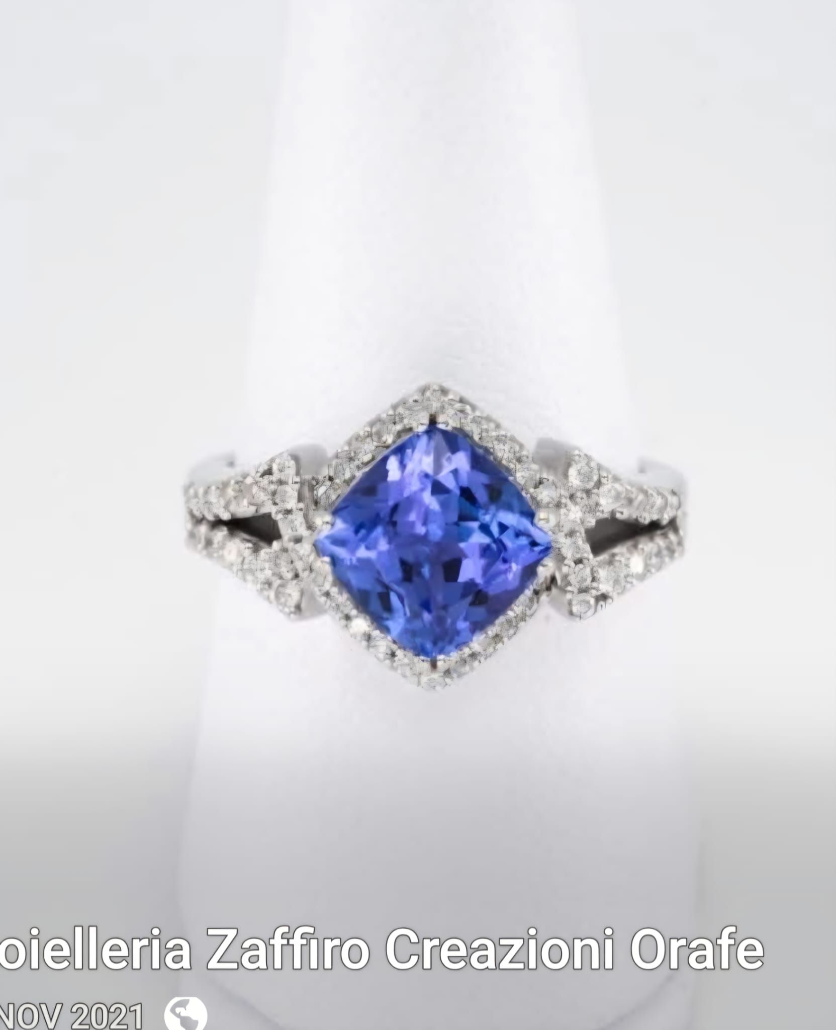 Anello di diamanti con pietra preziosa quadrata blu, incastonata su un dito bianco.
