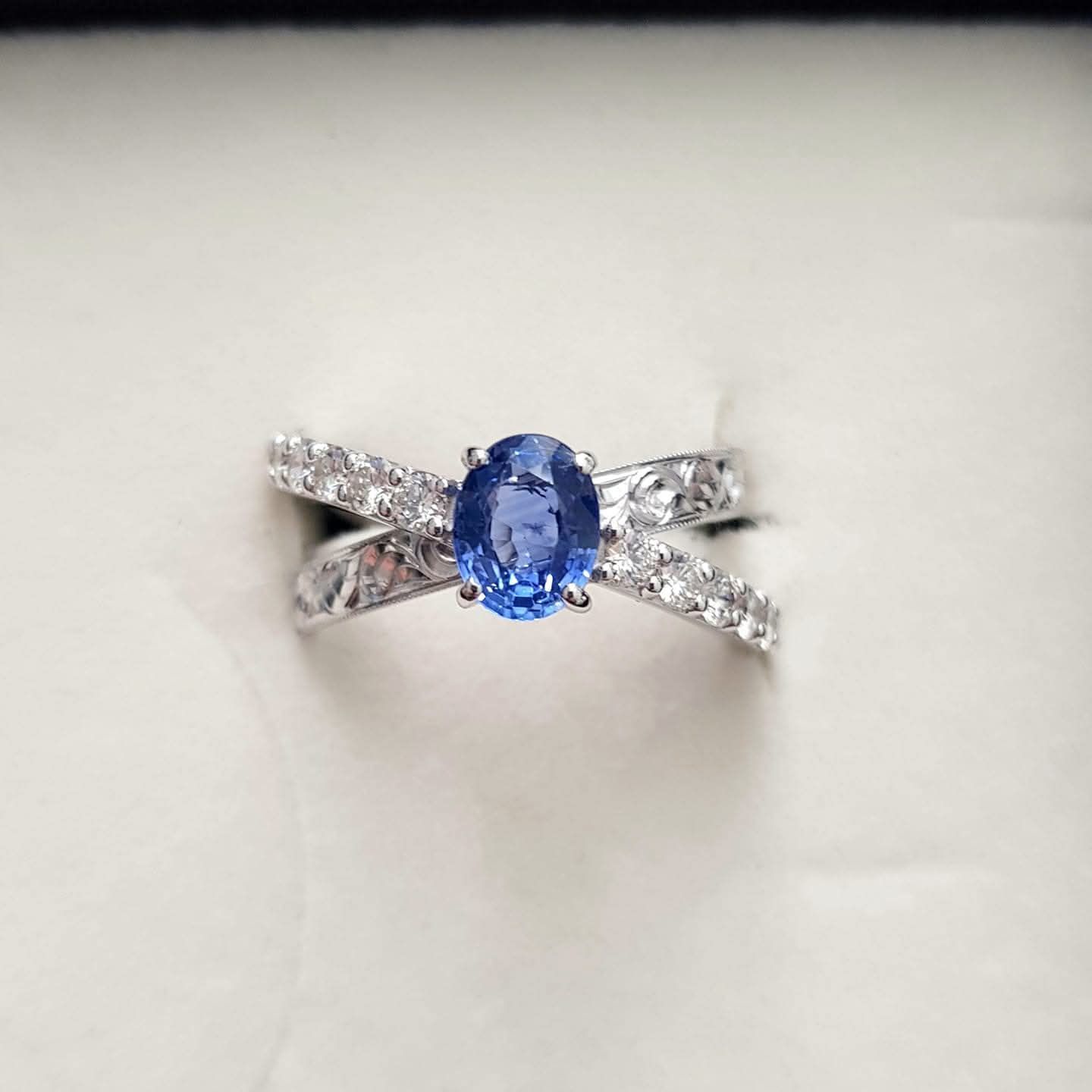 Anello con zaffiro con pietra centrale ovale blu e fascia di diamanti incrociati.
