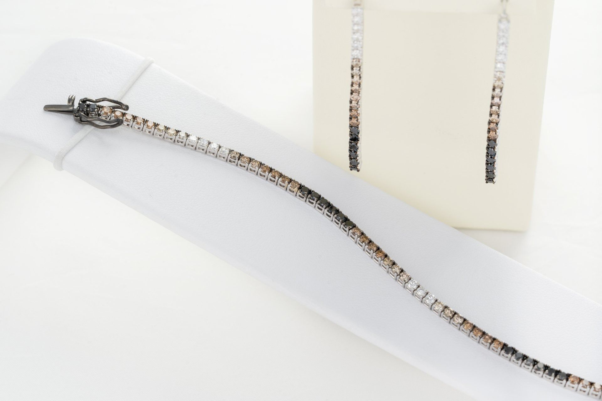 Un set di gioielli: un braccialetto e orecchini pendenti con maglie quadrate nere, dorate e argentate.